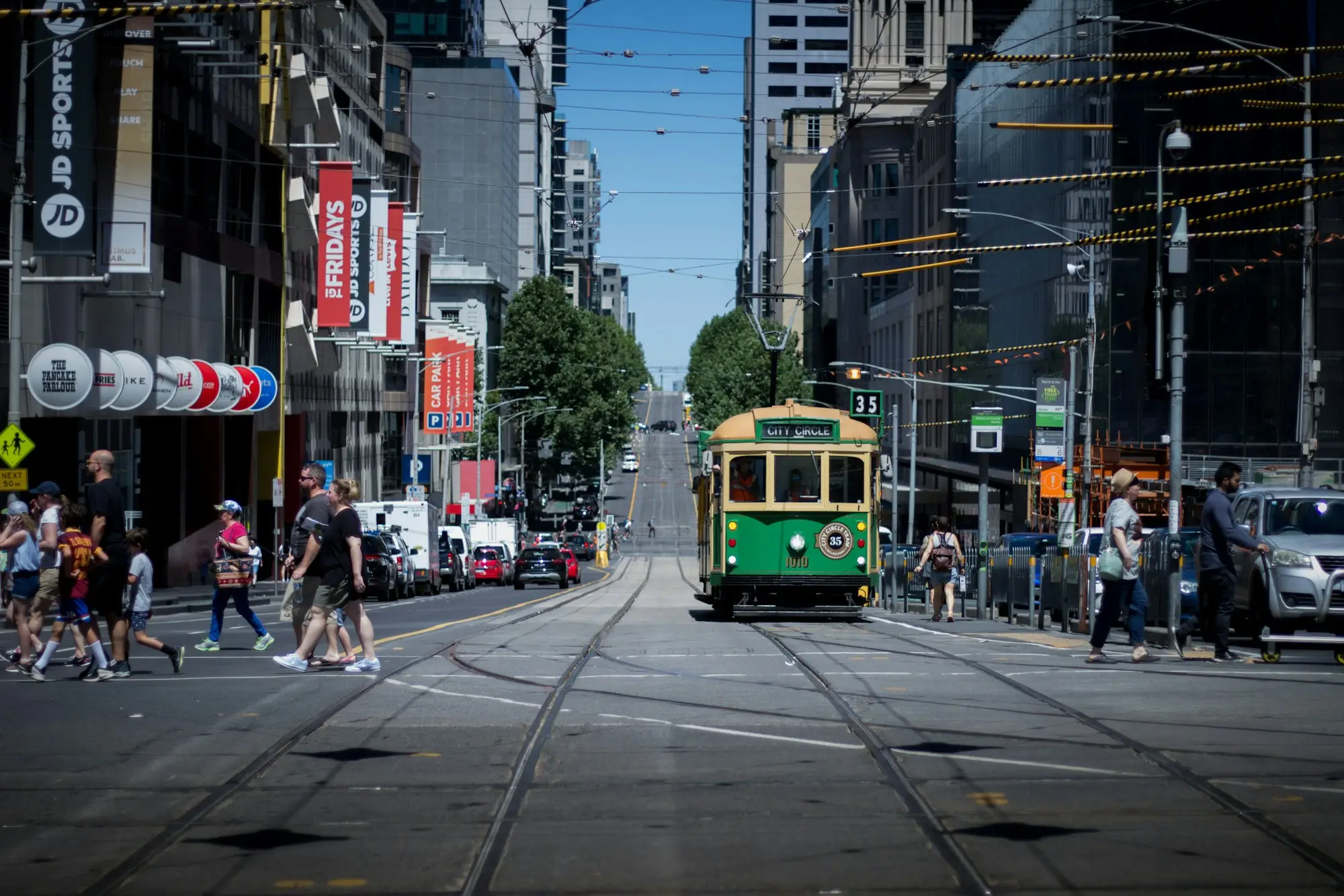 Green and yellow tram running down a busy Melbourne city street