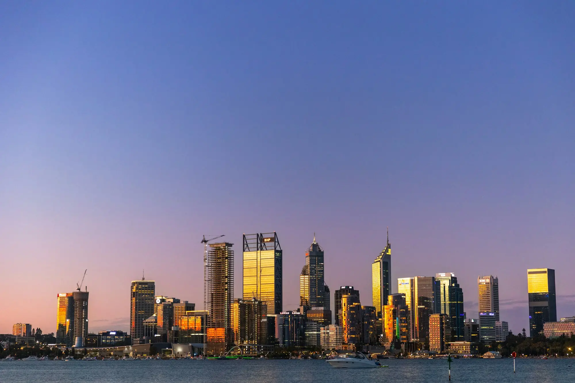 Perth city towers glowing at dusk across the Swan River