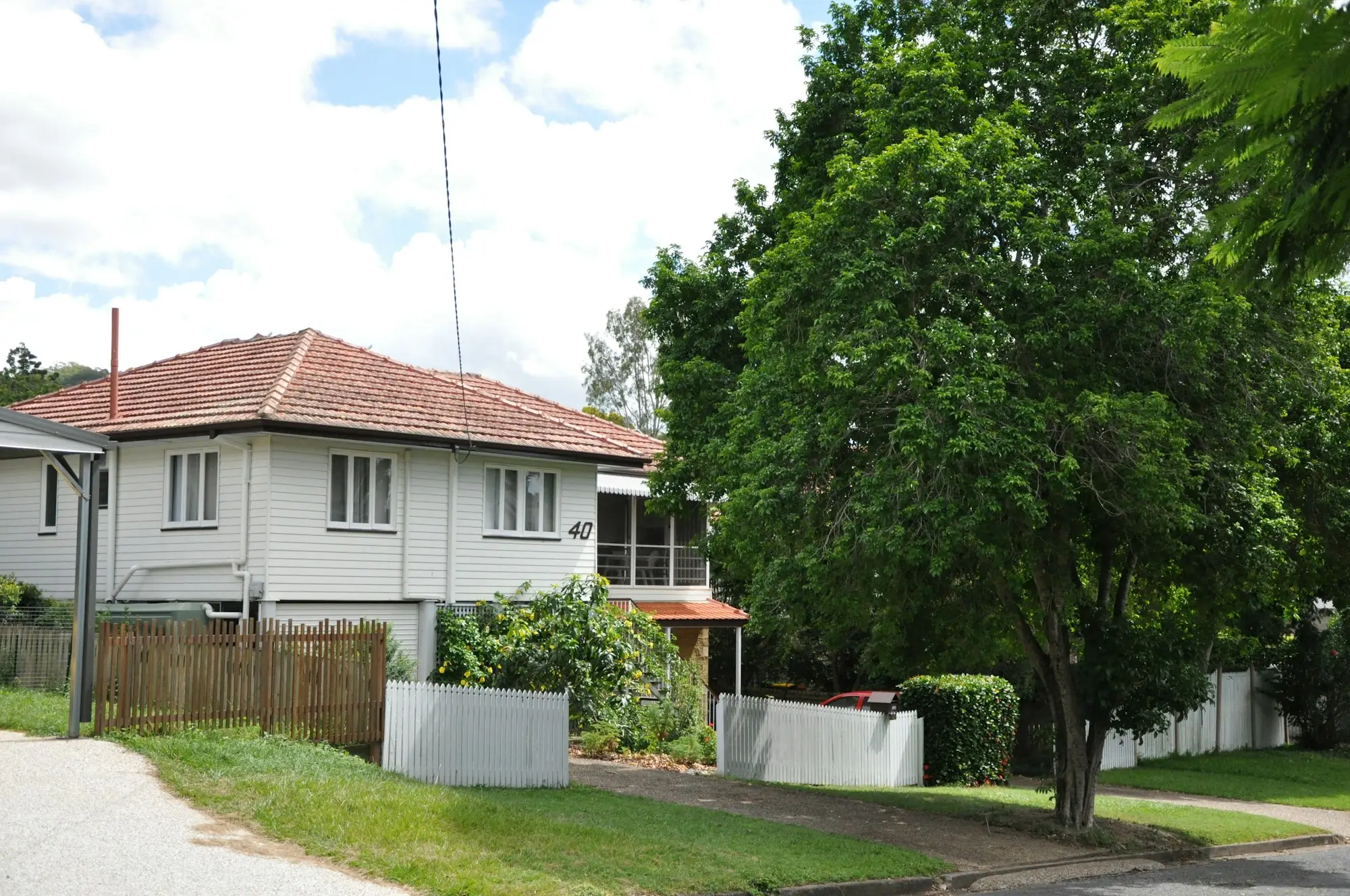 Raised Queenslander house with a red roof on a leafy Brisbane street